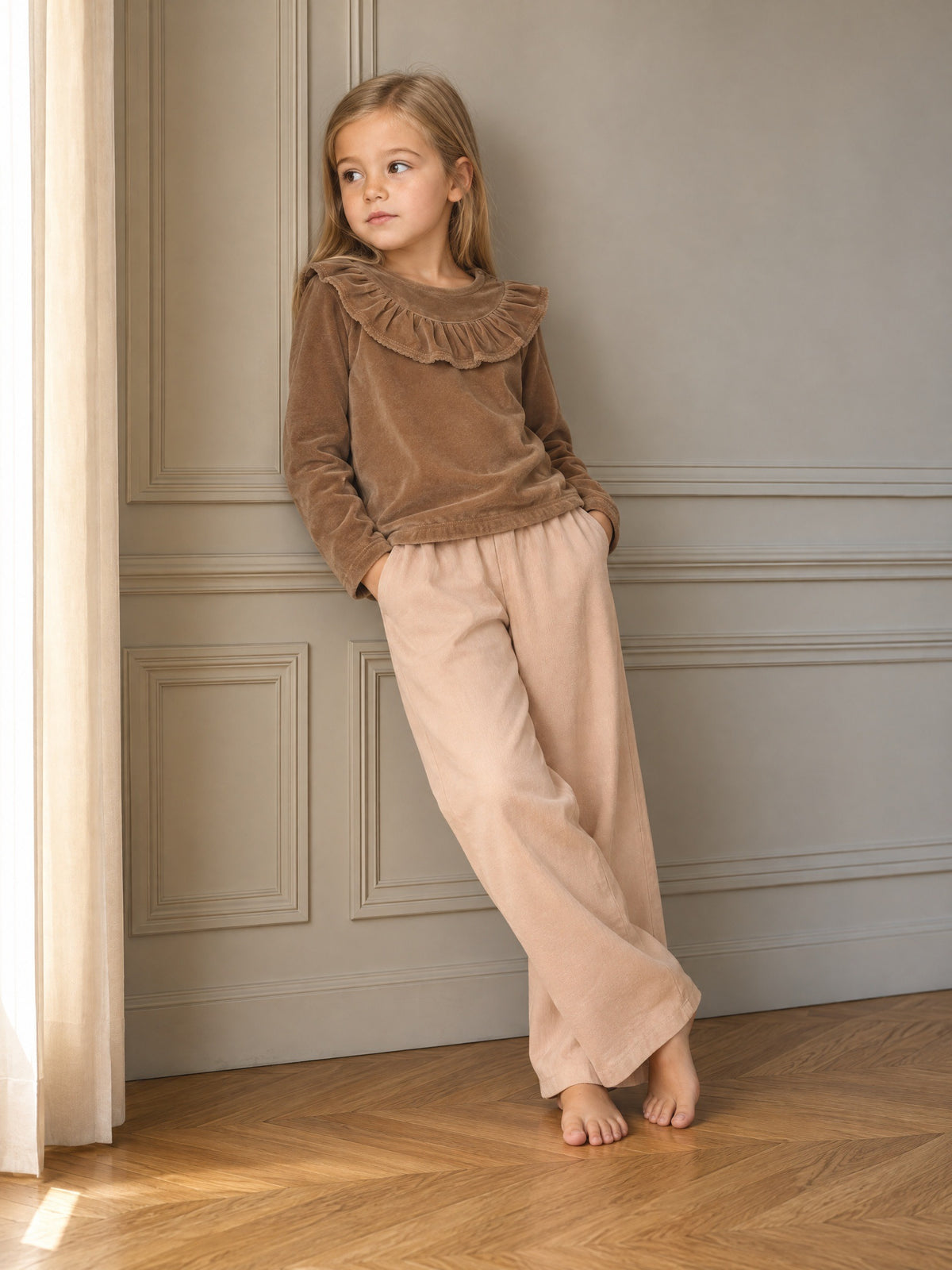 Child wearing a long-sleeve velour top with a ruffled Peter Pan collar and shoulder buttons